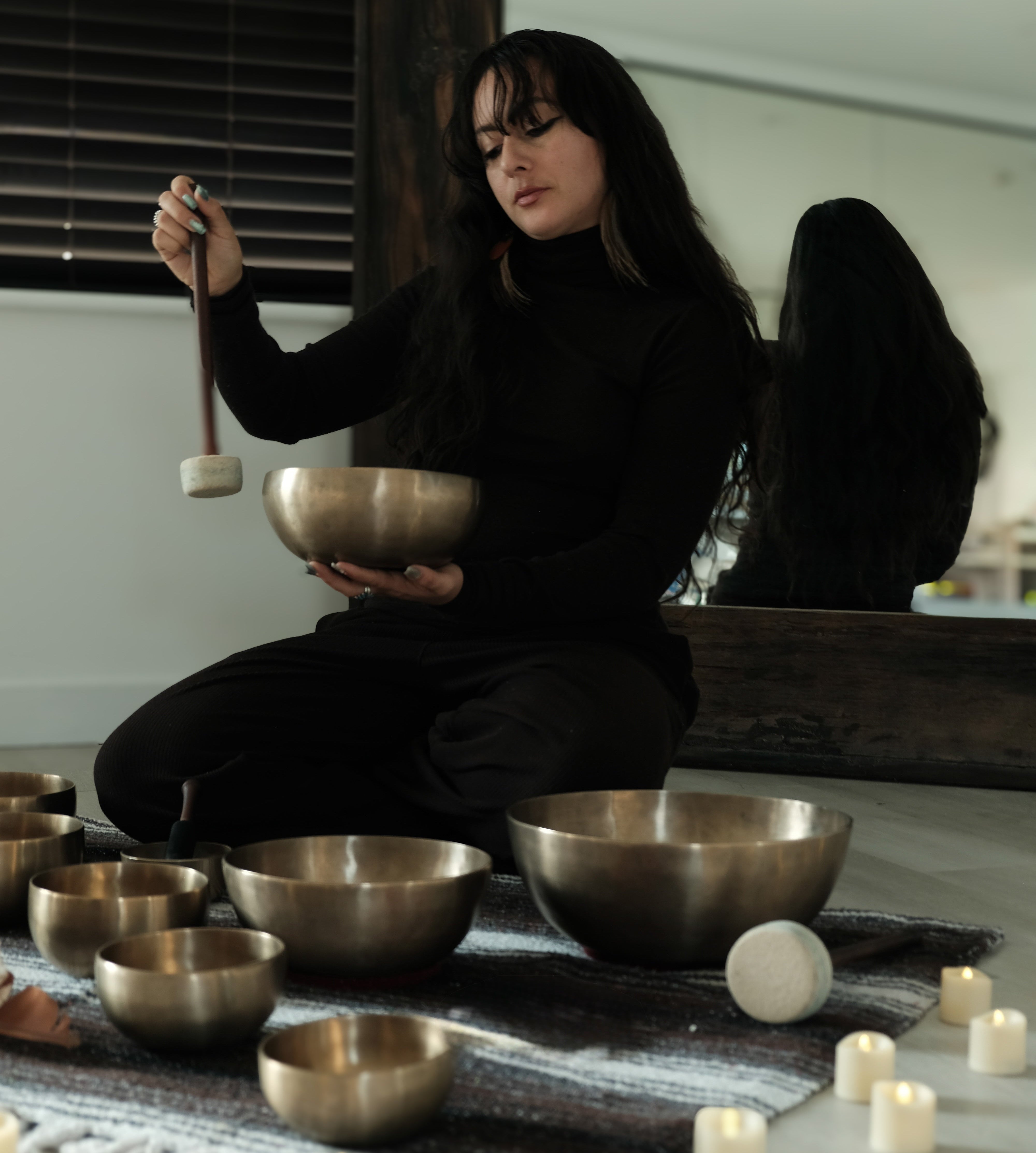 Person sitting on the floor with singing bowls and candles in a room.